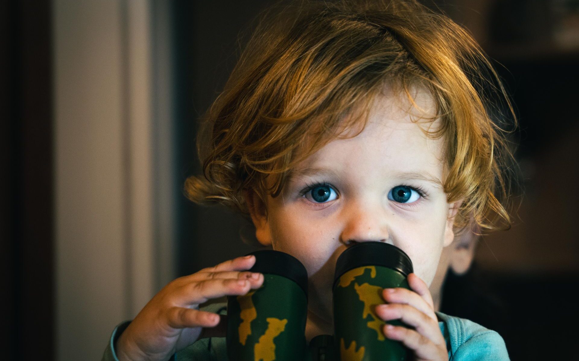 Toddler holding camouflage toy binoculars, a symbol of the digitally exposed generation and the future of clandestine HUMINT.