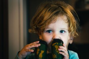 Toddler holding camouflage toy binoculars, a symbol of the digitally exposed generation and the future of clandestine HUMINT.